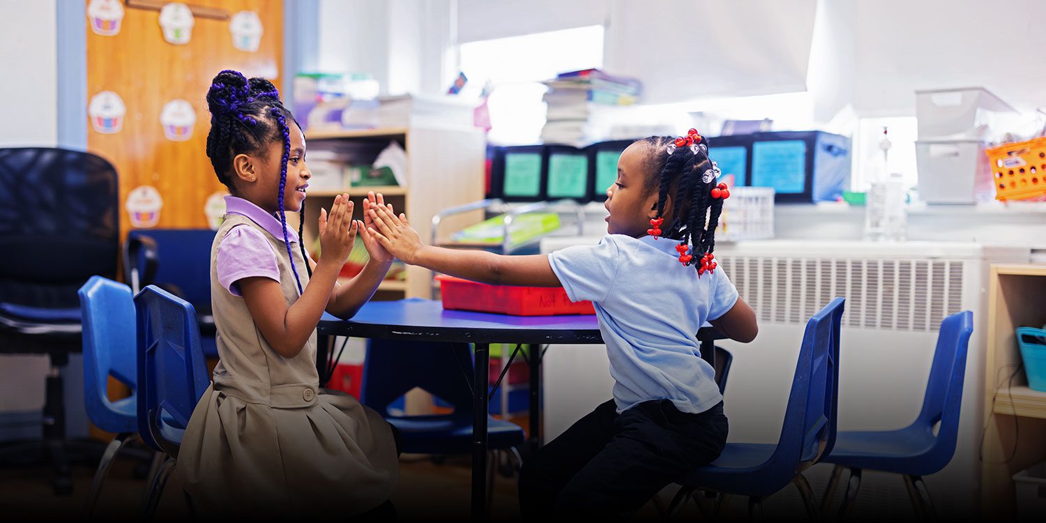 Students playing at a desk in a classroom.